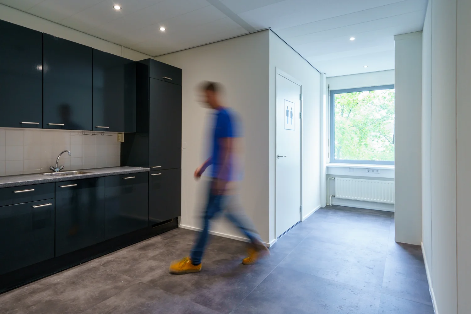 Een man loopt door een lichte gang met een moderne zwarte keuken aan de Baarnsche Dijk.